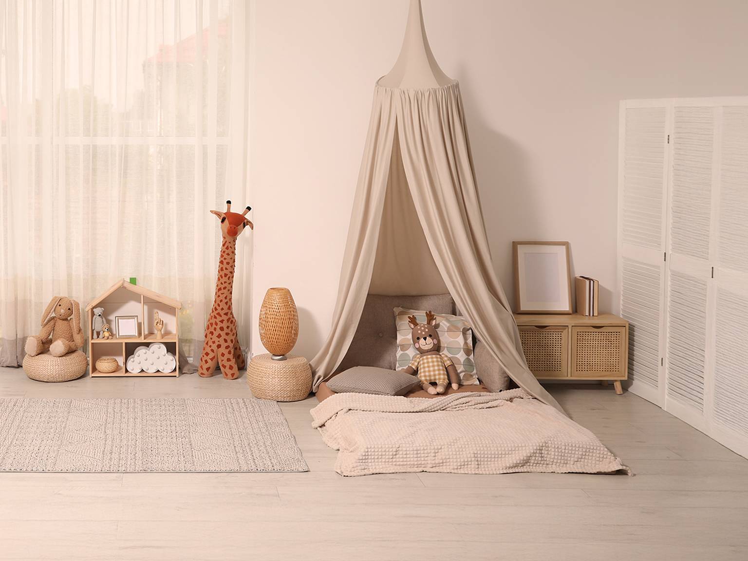 Gemütliches Kinderzimmer mit einem beigen Himmelbett, Stofftieren, einer Giraffenfigur, einer Korblampe und einem kleinen Schrank auf einem hellen Holzboden.