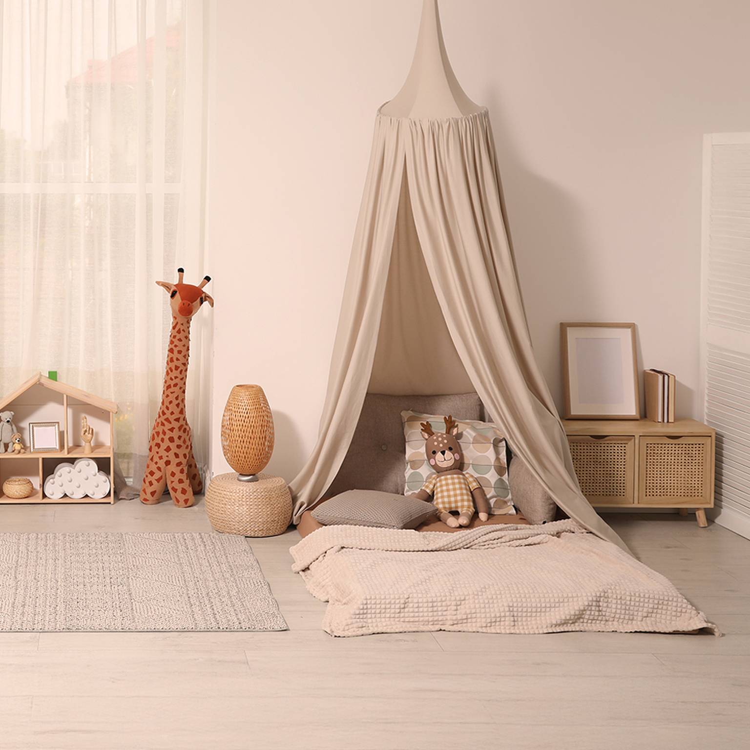 Gemütliches Kinderzimmer mit einem beigen Himmelbett, Stofftieren, einer Giraffenfigur, einer Korblampe und einem kleinen Schrank auf einem hellen Holzboden.