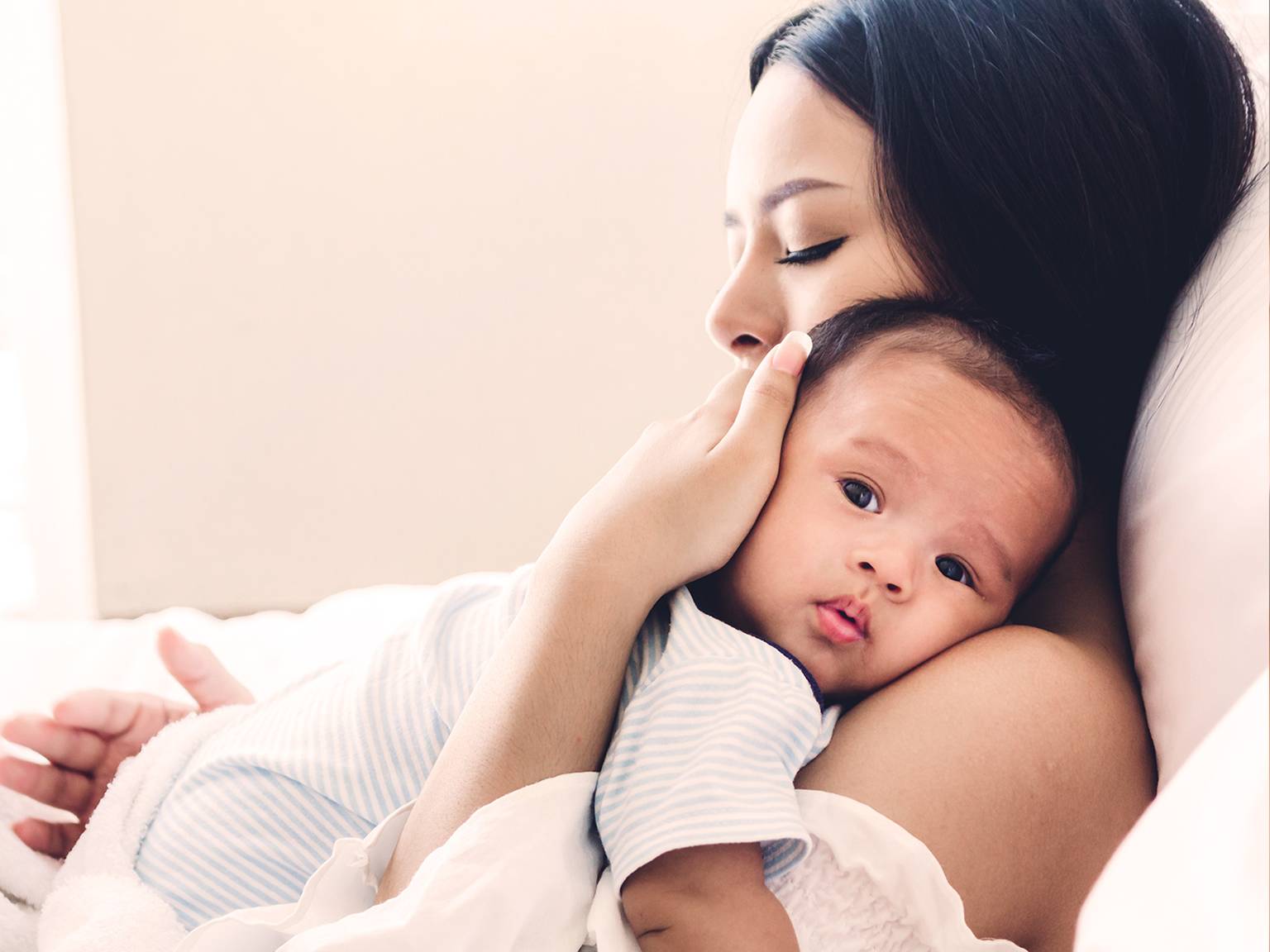 Eine Frau wiegt ein Baby sanft auf ihrer Brust, die Augen geschlossen, und strahlt damit Wärme und Zärtlichkeit aus. Das Baby sieht zufrieden und entspannt aus.