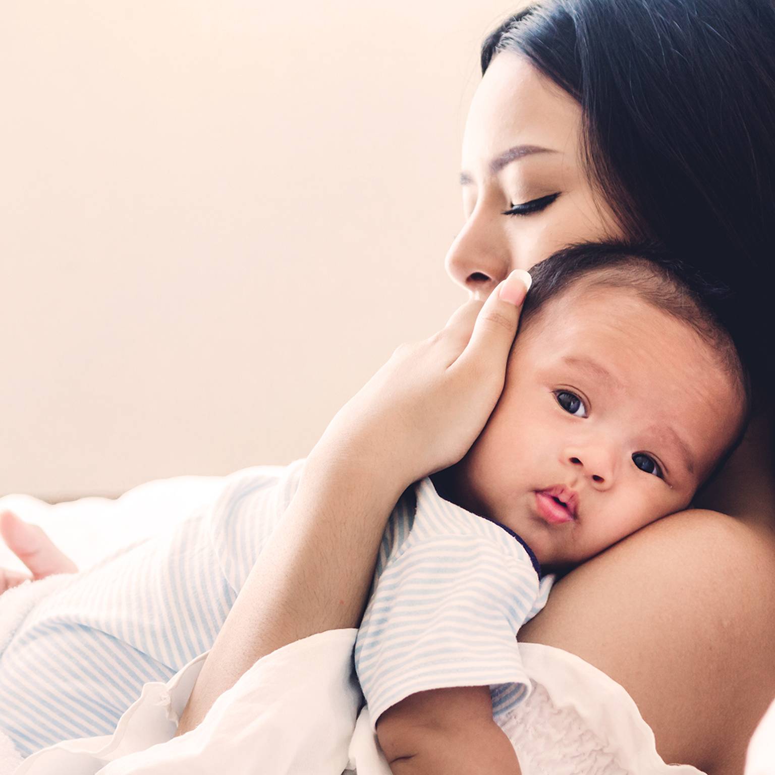 Eine Frau wiegt ein Baby sanft auf ihrer Brust, die Augen geschlossen, und strahlt damit Wärme und Zärtlichkeit aus. Das Baby sieht zufrieden und entspannt aus.