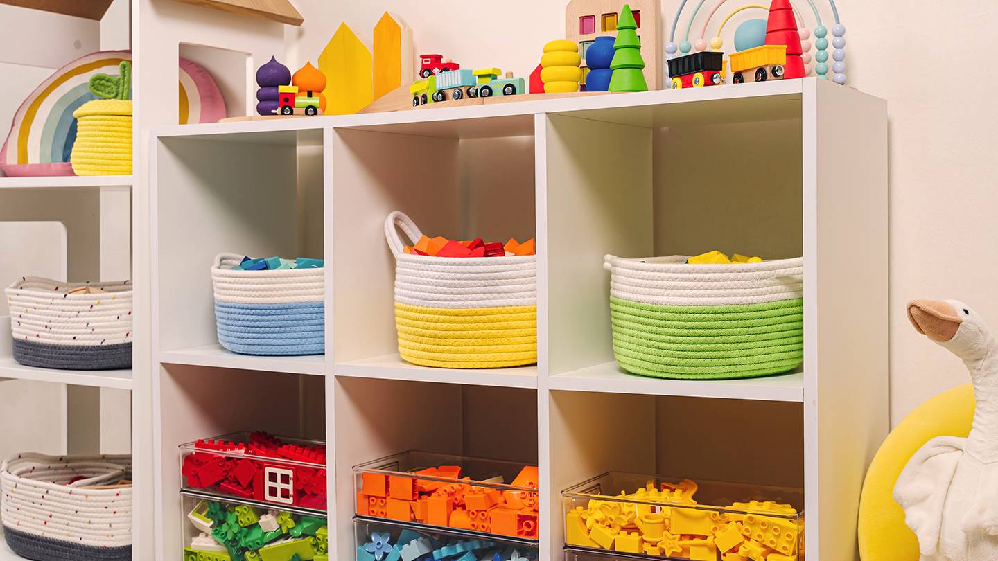 Ein farbenfrohes Kinderzimmerregal mit Körben voller Spielzeug, Blöcken und Spielzeugeisenbahnen, mit Gänseplüsch und Regenbogendekor.