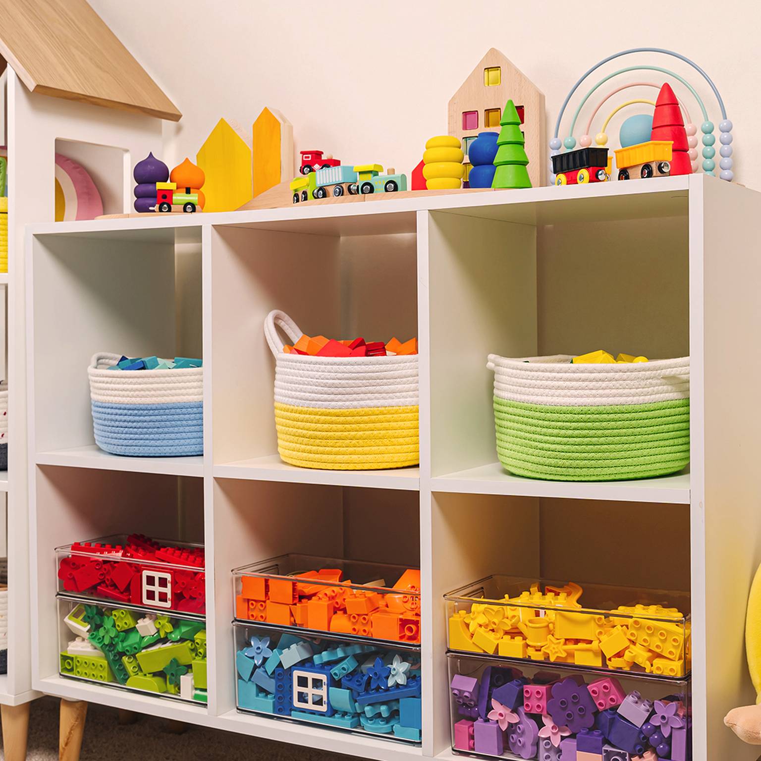Ein farbenfrohes Kinderzimmerregal mit Körben voller Spielzeug, Blöcken und Spielzeugeisenbahnen, mit Gänseplüsch und Regenbogendekor.