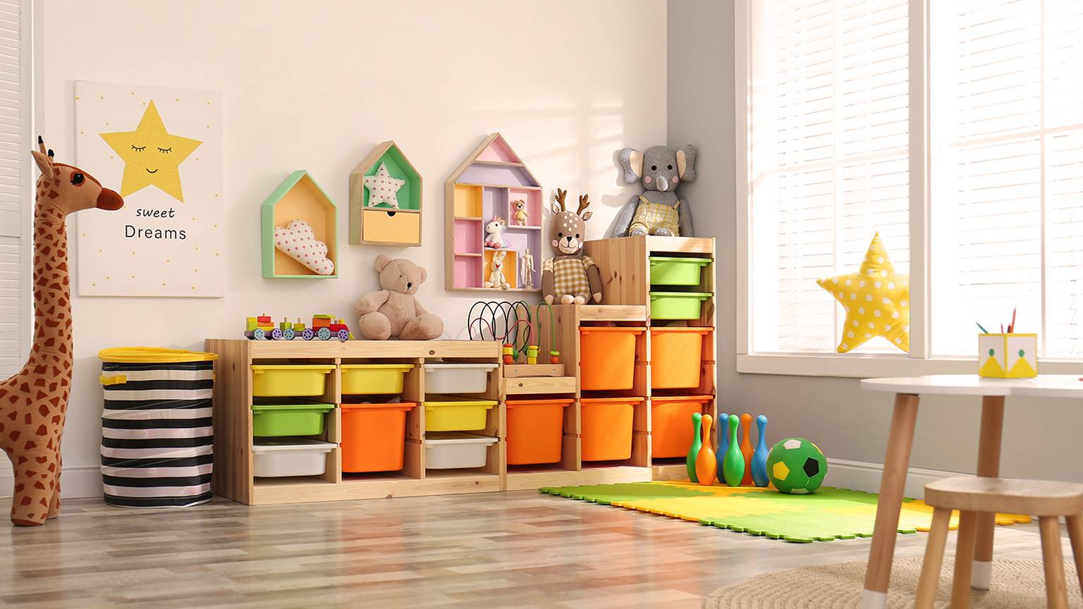 Helles Spielzimmer mit bunten Aufbewahrungsbehältern, Spielzeug, einem Giraffenplüschtier und Wanddekor. Sonnenlicht strömt durch große Fenster auf den Holzboden.