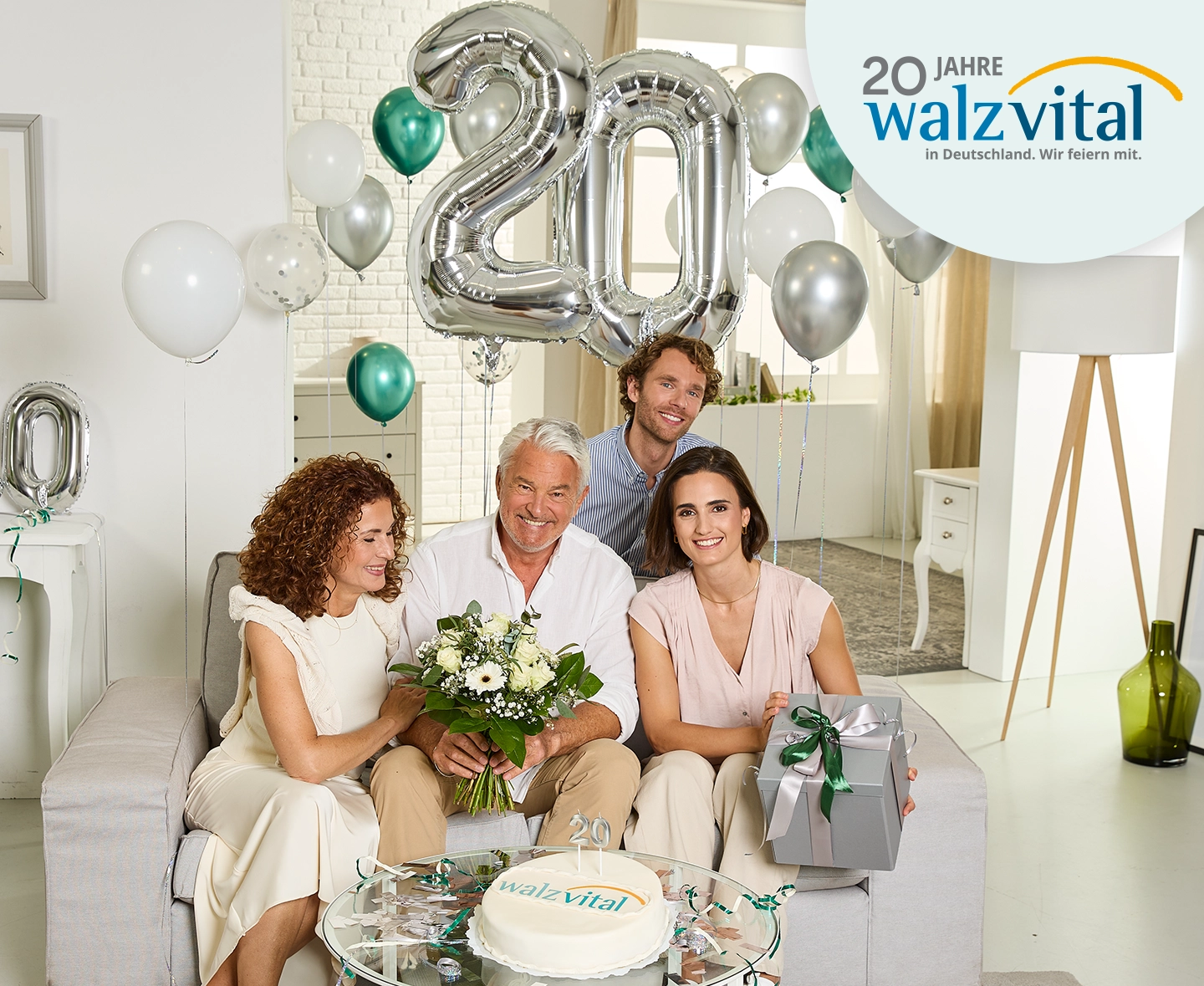 Vier Personen feiern das 20-jährige Jubiläum von Walzvital in einem hellen Raum mit Ballons, Blumen und einer Torte.