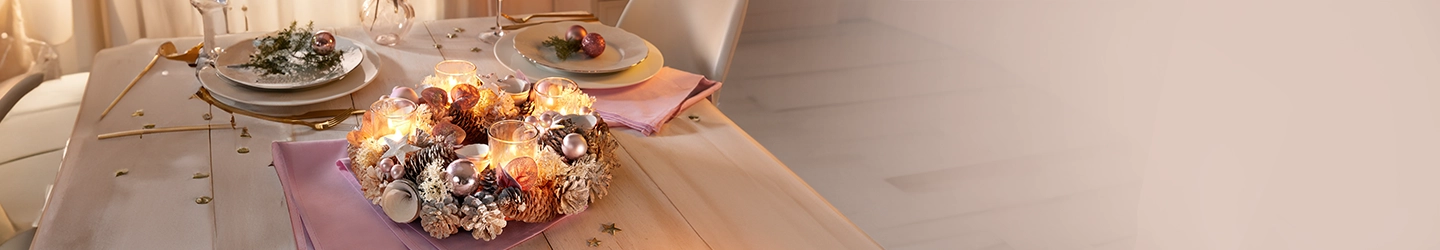 Festlich gedeckter Tisch mit Kerzenkranz, goldenem Besteck und Dekorationen. Stimmungsvolle Beleuchtung und elegante Servietten auf den Tellern.