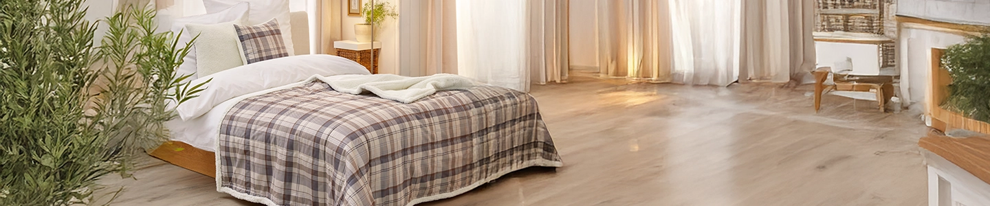 Gemütliches Schlafzimmer mit karierter Tagesdecke, Holzboden, Topfpflanzen und transparenten Vorhängen, die sanftes Tageslicht hereinlassen.