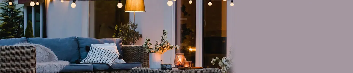 Gemütliche Terrasse mit Korbmöbeln, Kissen und Lichterketten. Ein kleiner Tisch mit Kerzen sorgt für eine warme Atmosphäre.