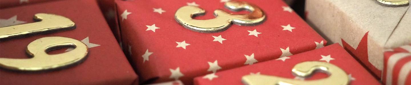 Nahaufnahme von rot-weißen, sternförmigen Geschenkboxen mit goldenen Zahlen darauf, die ein festliches und dekoratives Arrangement bilden.