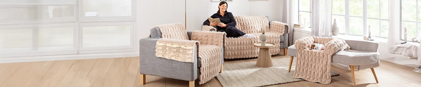 Frau liest auf einem beigen Sofa mit strukturierten Bezügen, umgeben von modernen Möbeln und einem kleinen Hund, in einem hellen, gemütlichen Wohnzimmer.