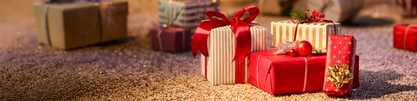 Mehrere mit rot gestreiftem Papier verpackte Geschenke, verziert mit Schleifen und Ornamenten, liegen auf einem Teppichboden.