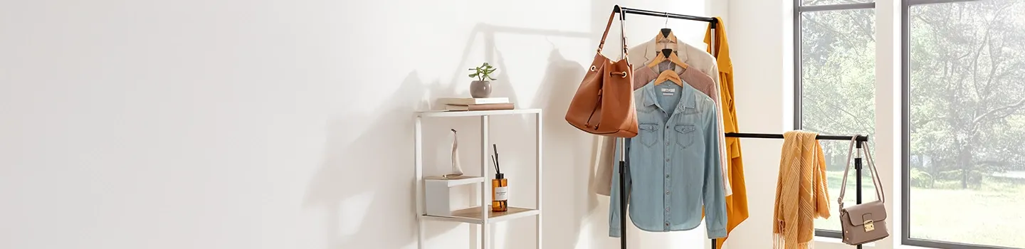 Kleiderständer mit Jeanshemden, Jacken, Schals und Handtaschen in der Nähe großer Fenster in einem hellen Raum.