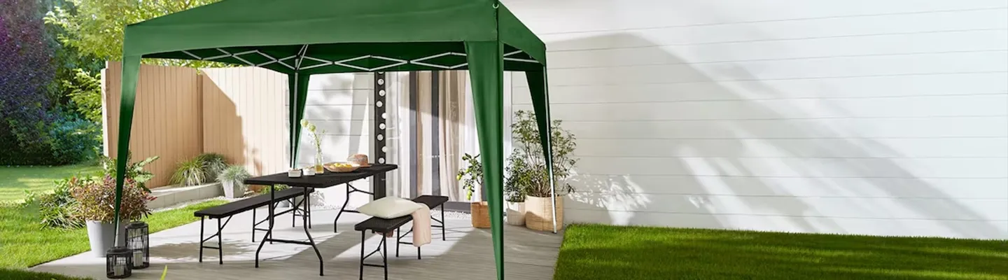 Terrasse im Freien mit grünem Pavillon, Holztisch, Bänken mit Kissen, umgeben von Pflanzen und Gras