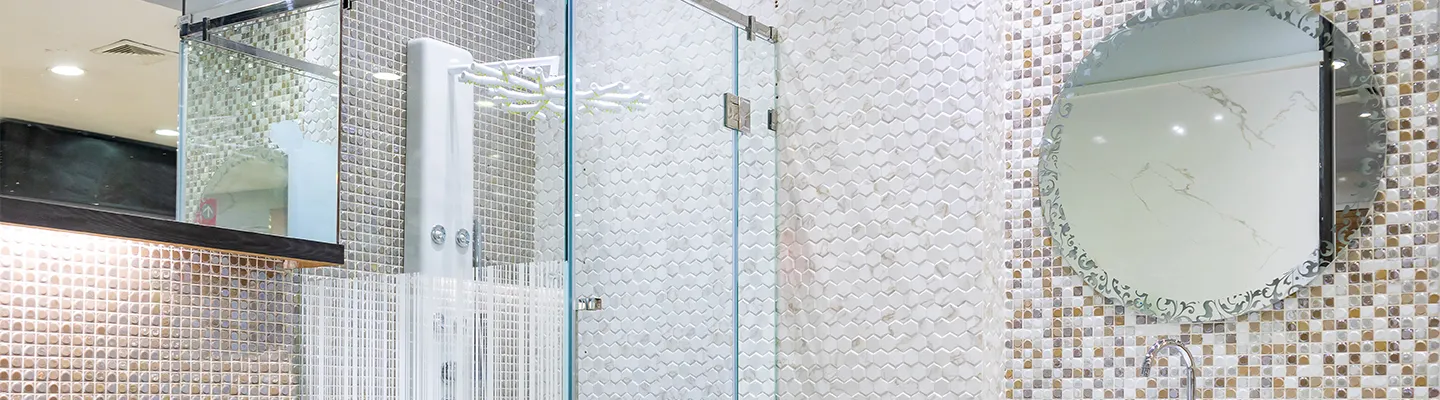 Modernes Badezimmer mit einer Glasdusche, Mosaikfliesen und einem runden Spiegel, der Licht widerspiegelt.