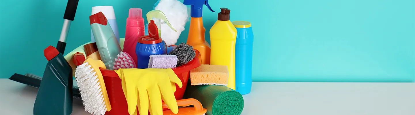 Reinigungsmaterialien auf einem blauen Hintergrund, darunter Handschuhe, Schwämme, eine Sprühflasche und Mikrofaser-Tücher.