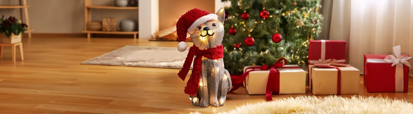 Beleuchtete Weihnachtskatze mit Mütze und Schal vor Weihnachtsbaum und Geschenken.