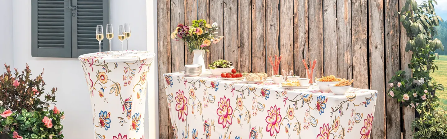 Ein mit Blumenmuster gestaltetes Tischarrangement mit Vorspeisen, kleinen Tellern, Blumen und Champagnergläsern vor einem rustikalen Holzhintergrund.