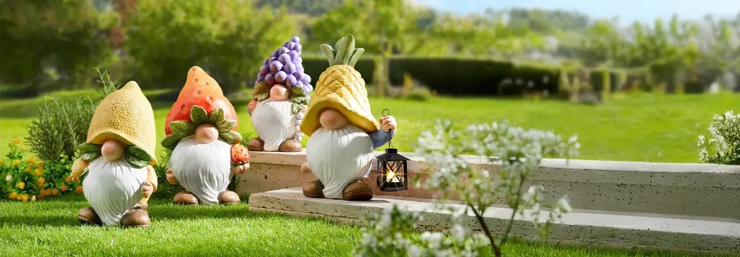 Vier Gartenzwerge mit fruchtförmigen Hüten – Ananas, Erdbeere, Traube und Mais – stehen auf einem üppigen Rasen nahe steinerner Stufen, wobei einer eine Laterne hält.