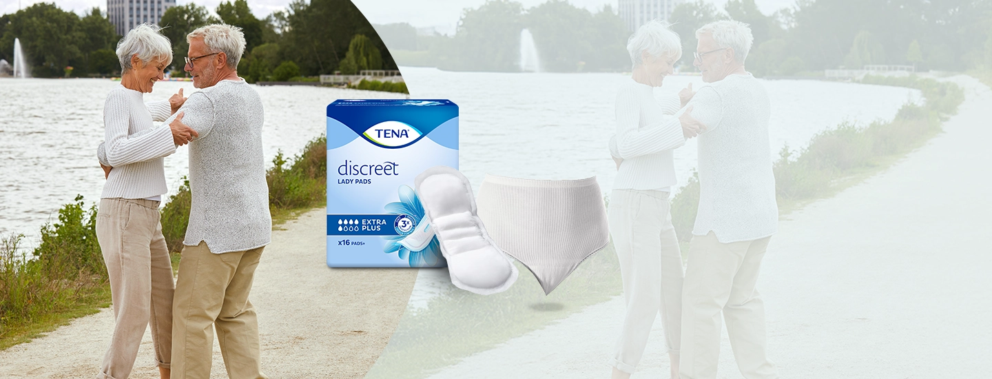 Älteres Paar tanzt am Seeufer, neben ihnen eine Packung TENA Discreet Damenbinden und ein Inkontinenzslip.