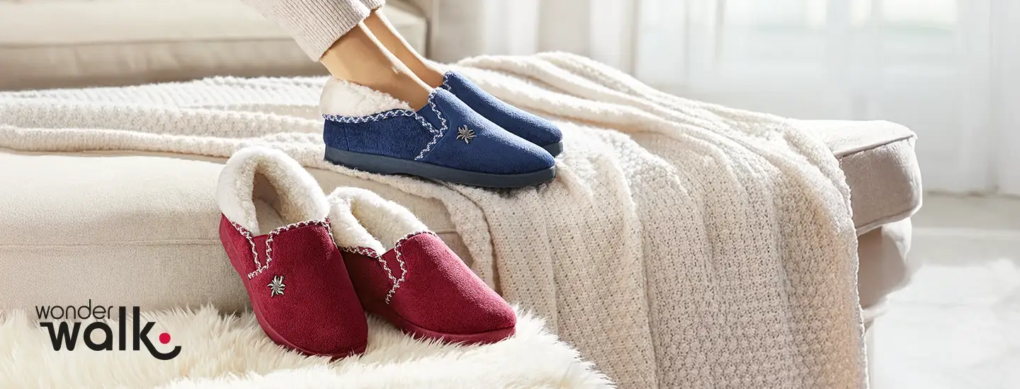 Eine Person mit blauen Pantoffeln neben roten Pantoffeln auf einer kuscheligen, cremefarbenen Decke.