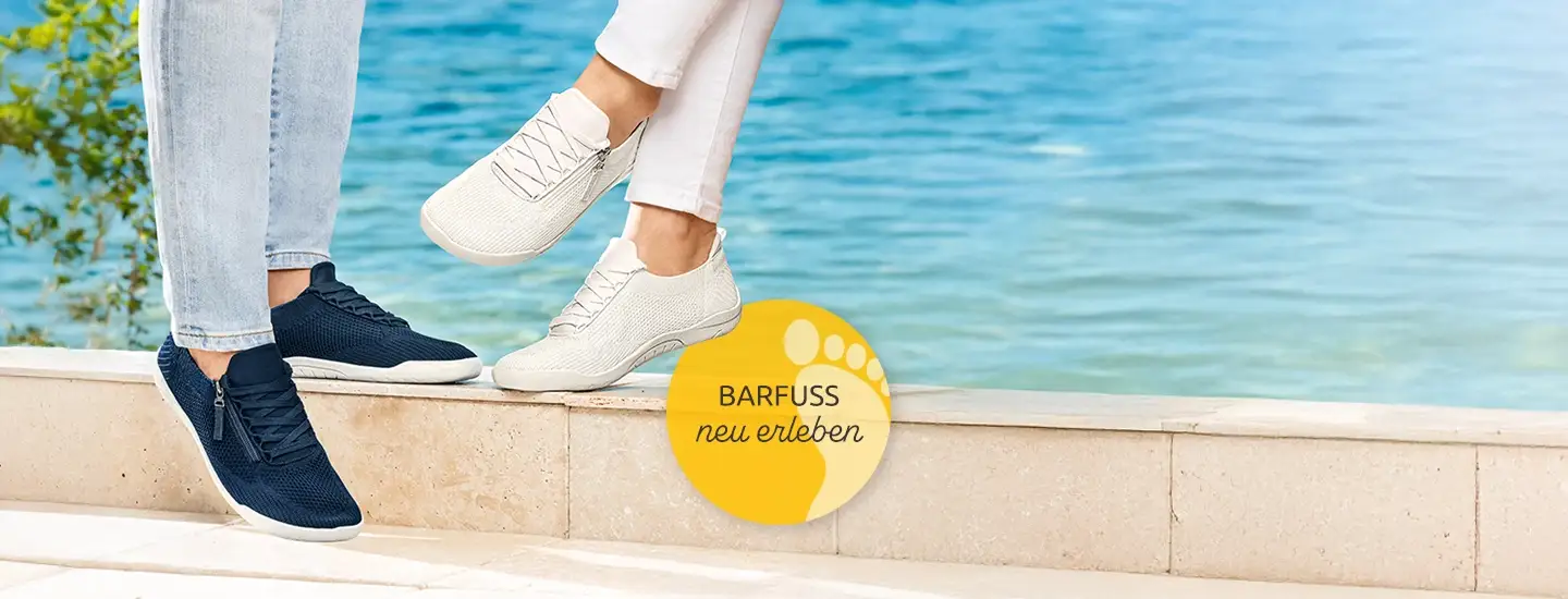 Zwei Personen in Freizeitschuhen sitzen am Wasser; eine trägt weiße Schuhe, die andere marineblaue. Auf dem runden Logo steht „Barfuss neu erleben“.
