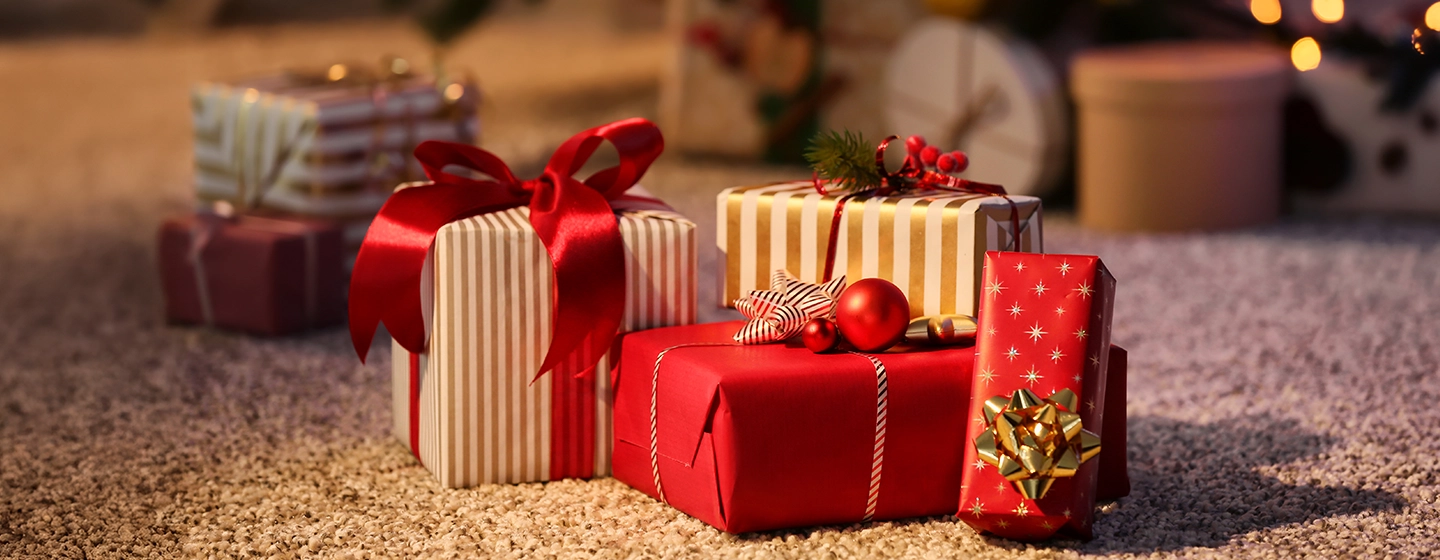 Weihnachtsgeschenke, verpackt in rot gestreiftem Papier, verziert mit Bändern und Ornamenten, auf einem Teppichboden platziert.