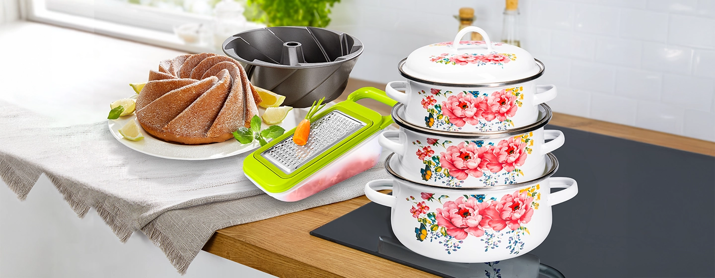 Eine Küchenszene mit auf einem Herd gestapelten Blumentöpfen, einem Gugelhupf-Kuchen mit Zitronenscheiben, einer Gugelhupf-Form und einer Reibe auf einer Arbeitsplatte mit einer Stoffabdeckung.