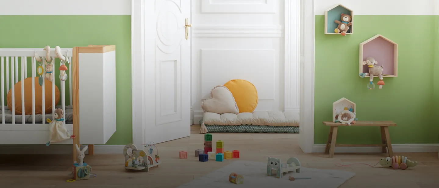 Ein gemütliches Kinderzimmer mit grünen Wänden, einem Kinderbett, Spielzeug und Regalen. Weiche Kissen und bunte Bauklötze liegen verstreut auf dem Holzboden.
