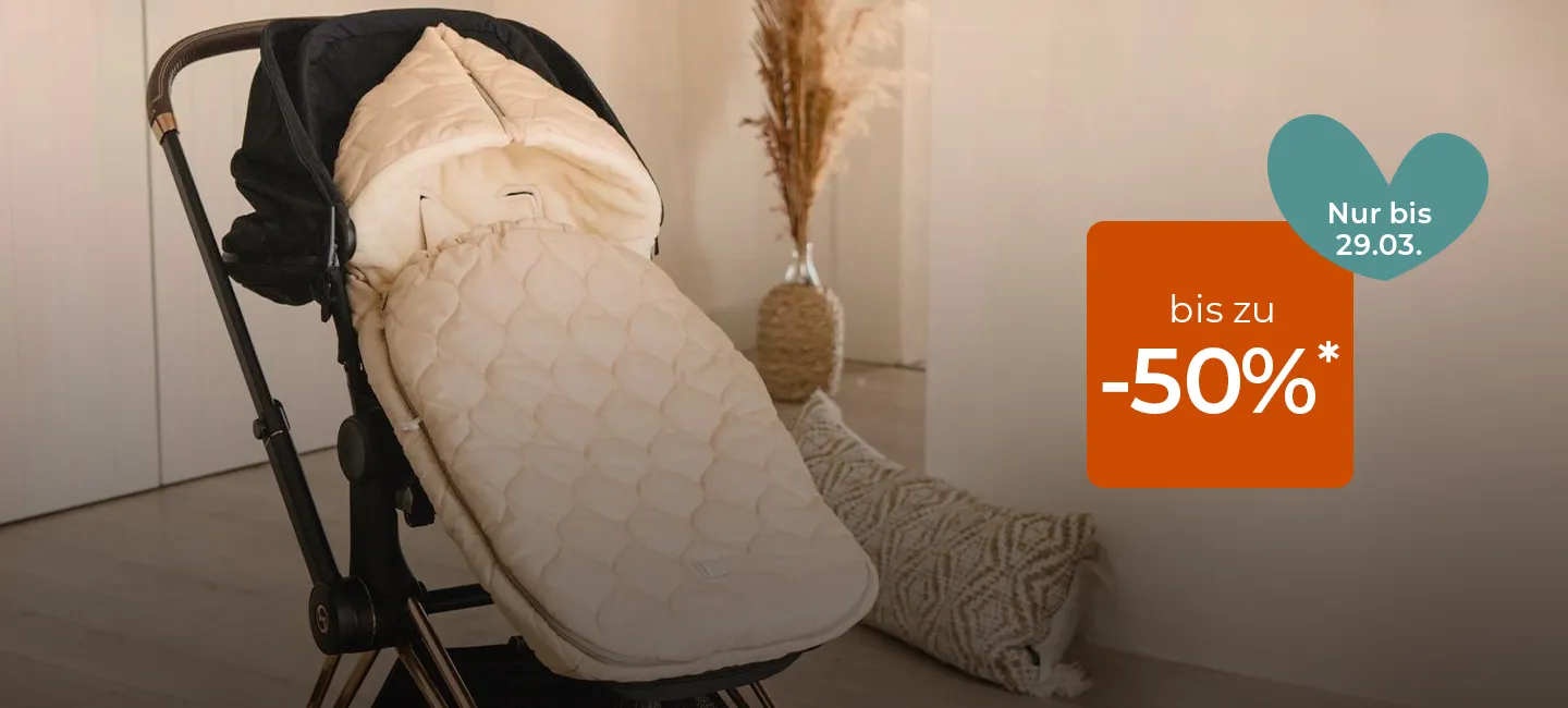 Ein cremefarbener Kinderwagen mit gepolstertem Bezug steht auf einem Teppich neben einer beigen Wand. Ein orangefarbenes Schild weist darauf hin, dass das Angebot „bis zu -50%*“ gültig bis zum 29.03. ist.