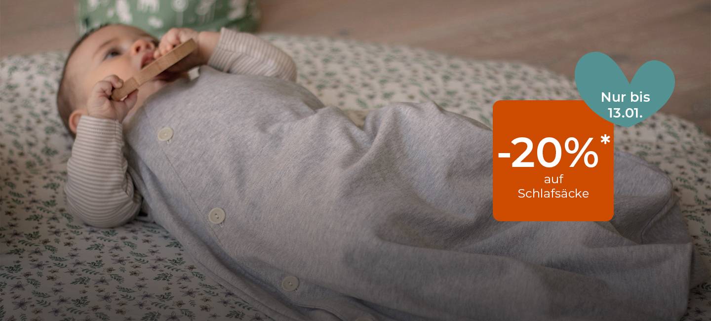 Baby liegt in einem grauen Schlafsack auf einer geblümten Matte und hält einen Beißring. Texteinblendung: „Nur bis 13.01. -20 %* auf Schlafsäcke.“