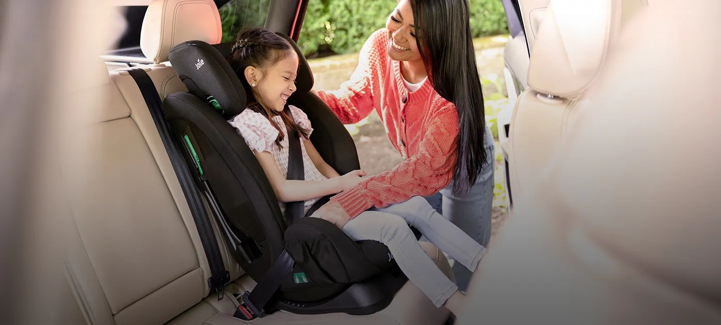 Eine Frau sichert ein lächelndes Kind in einem Kindersitz in einem Fahrzeug; beide scheinen glücklich und zufrieden zu sein.