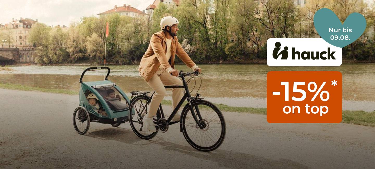 Mann fährt mit dem Fahrrad an einem Fluss entlang und zieht einen Kinderanhänger mit zwei Kindern. Ein Werbetext für ein 15%-Rabattangebot von Hauck ist eingeblendet.