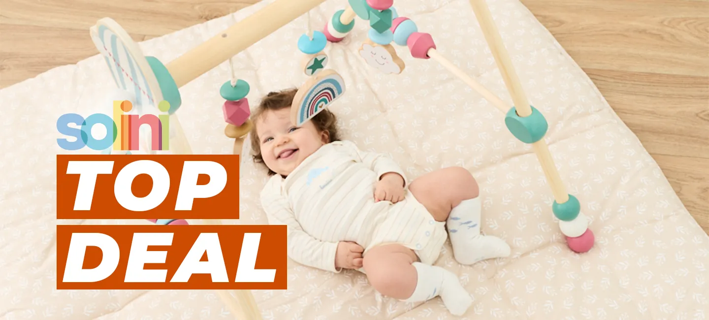 Ein Baby im Strampler lächelt unter einem hölzernen Spielbogen auf einer gepolsterten Matte. Auf dem Bild ist der Schriftzug „Solini Top Deal“ zu sehen.