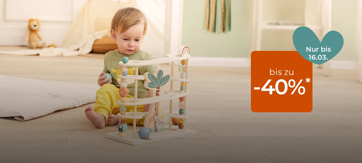 Ein Kleinkind spielt drinnen mit einer Murmelbahn, daneben ein Schild mit einem Rabattangebot von bis zu 40 % Ermäßigung, gültig bis zum 16. März.