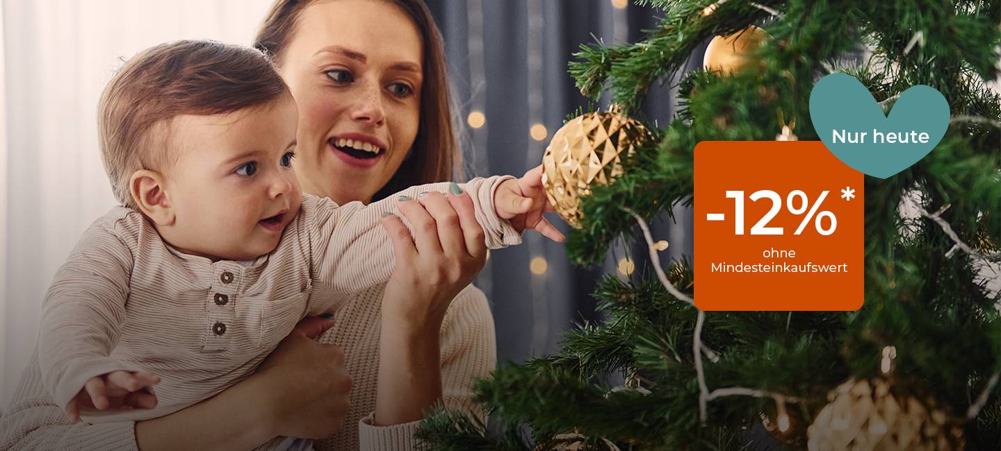 Frau hält ein Baby und greift nach einem geschmückten Weihnachtsbaum; Blaugrünes Herz und orangefarbener Anhänger mit der Aufschrift „Nur heute -12 % ohne Mindesteinkaufswert.“