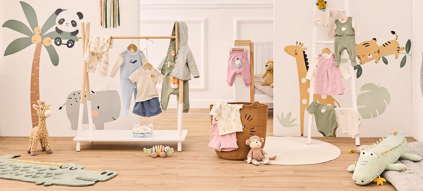 Eine Kinderzimmerszene mit tropischer Tiermotivdekoration und Babykleidung, mit Giraffen, einem Panda, einem Tiger und Krokodilmotiven an den Wänden.