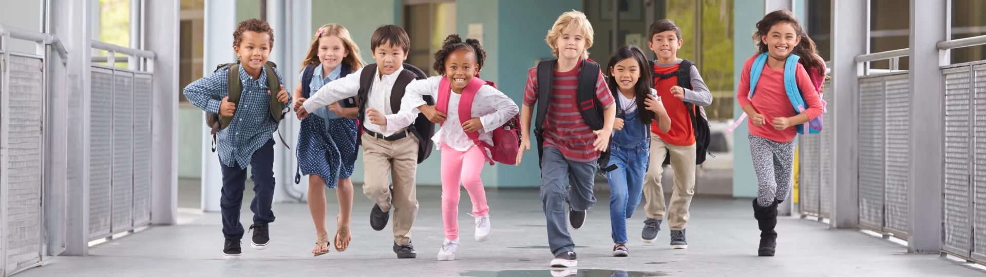 Eine Gruppe fröhlicher Kinder mit Rucksäcken rennt über den Schulweg und drückt dabei Begeisterung und Energie aus.