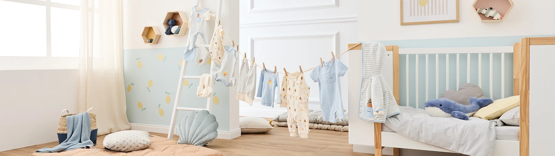 Ein gemütliches Kinderzimmer mit einem Kinderbett, pastellfarbener Kleidung an einer Leine und Kuscheltieren. Die Wände sind hellblau und weiß gestrichen.