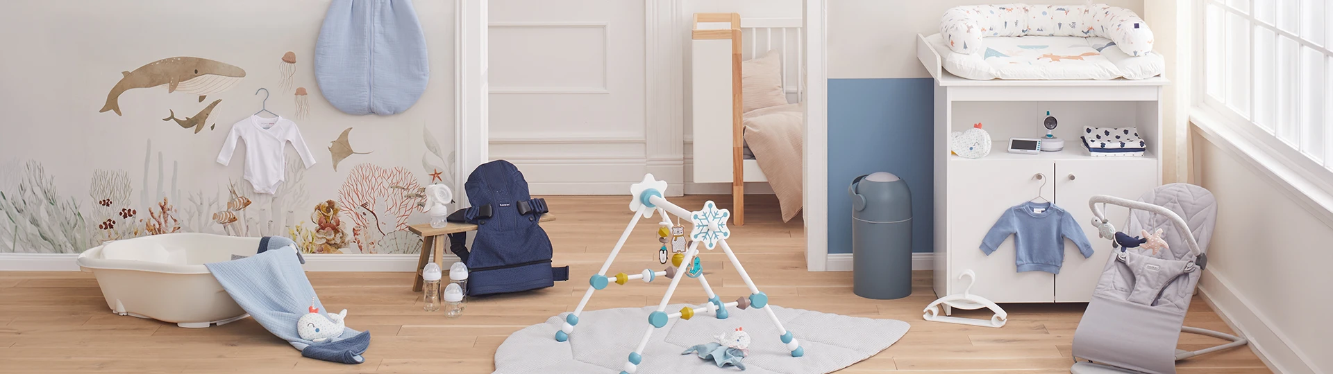 Ein gemütliches Kinderzimmer mit Babybett, Wickeltisch, Babywippe, Badewanne und Spielbogen. Maritime Dekoration mit Wandbildern und blauen Akzenten.