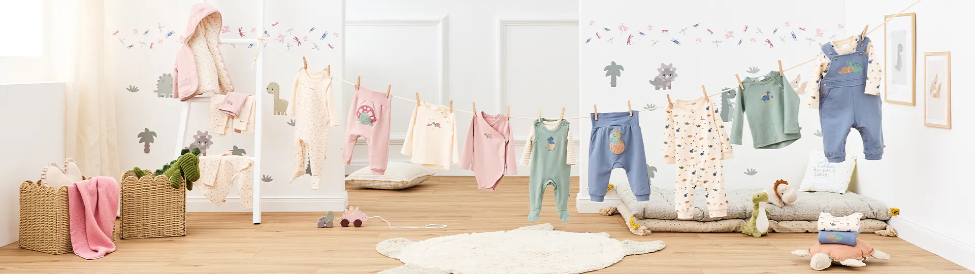 Ein Kinderzimmer mit auf einer Leine aufgehängter Babykleidung, umgeben von gemütlicher Dekoration, Plüschtieren, Rattan-Körben und Wandaufklebern mit Dinosauriermotiven.