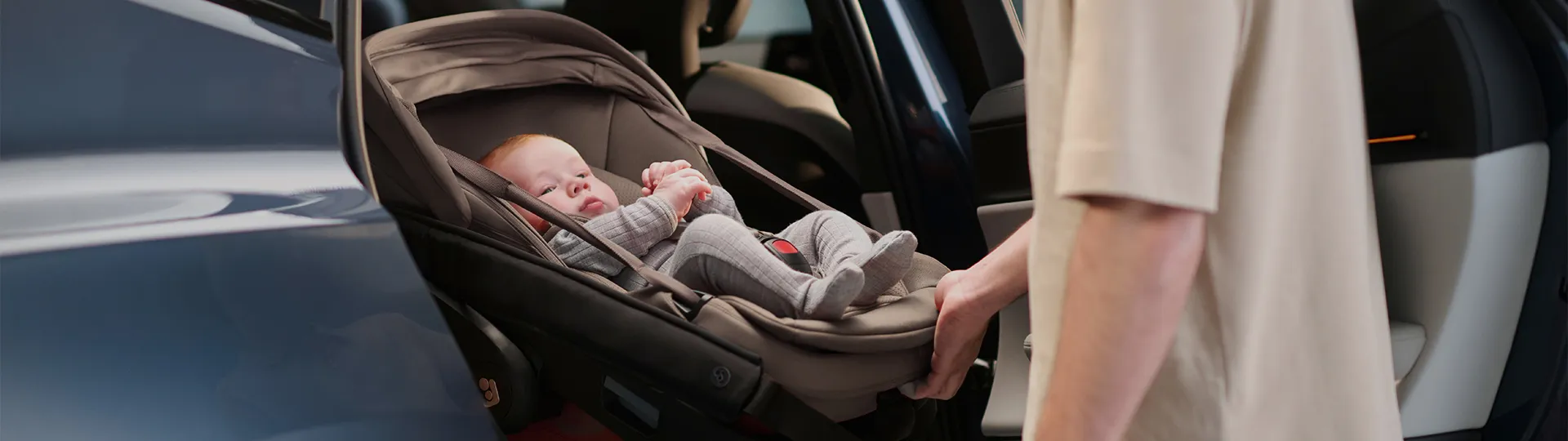 Ein Baby in grauer Kleidung ist sicher in einem Kindersitz angeschnallt, der in ein Fahrzeug verladen wird.