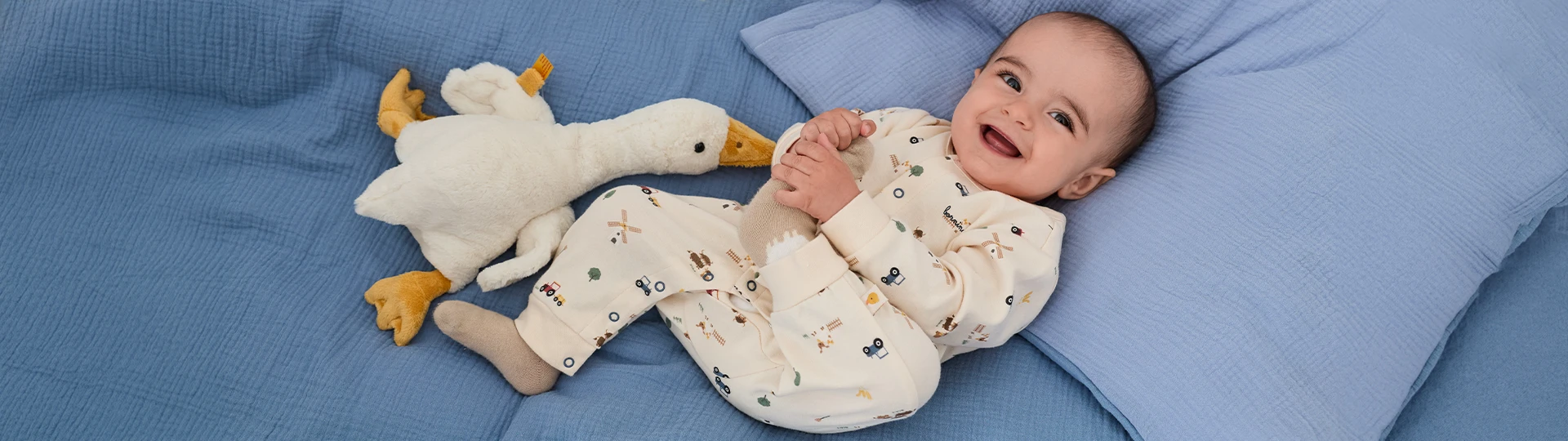 Ein Baby liegt im Bett neben einem Kuscheltier