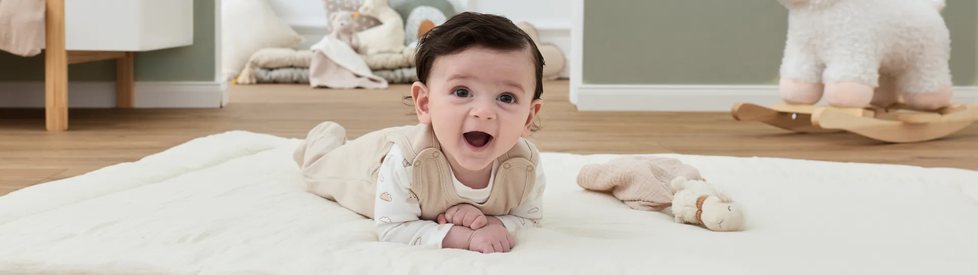 Ein lächelndes Baby in einem hellen Strampler liegt auf einer weichen Decke in einem gemütlichen Zimmer mit Spielzeug und Kinderzimmerdekoration.