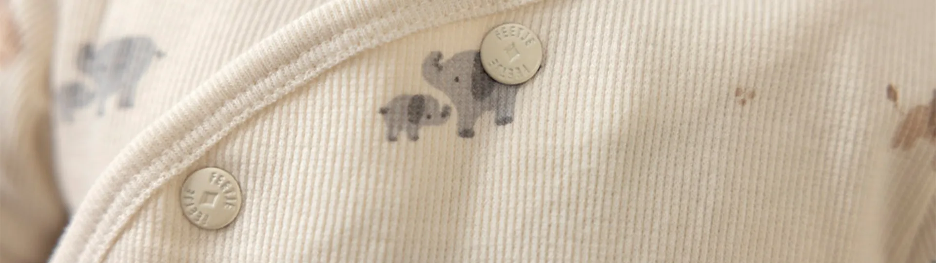Nahaufnahme eines cremefarbenen Baby-Outfits aus geripptem Stoff mit aufgedruckten Elefanten und Druckknöpfen.