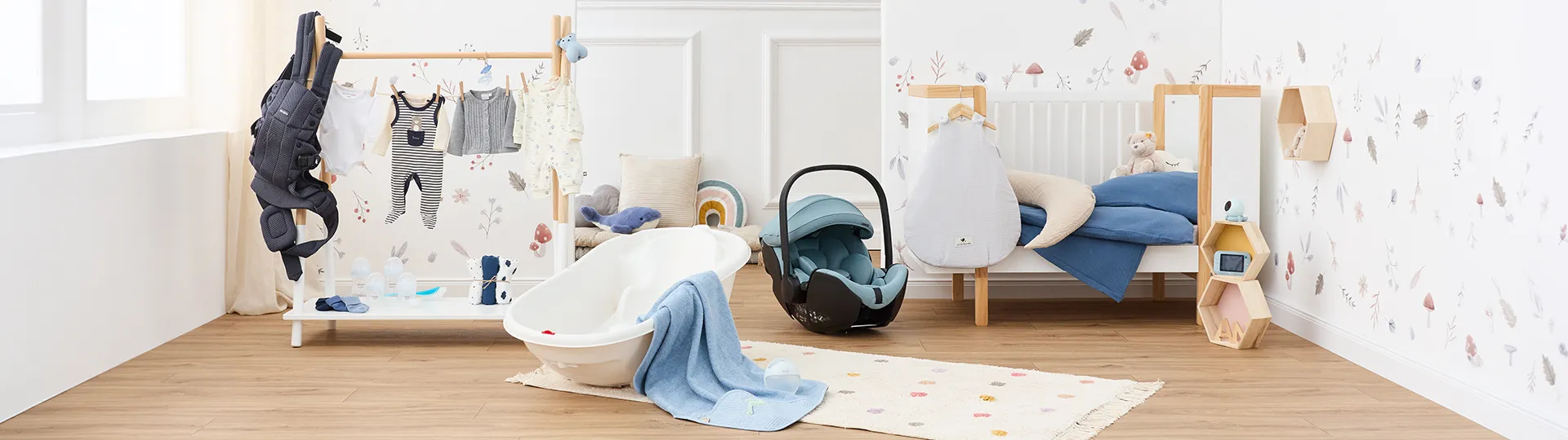 Helles Kinderzimmer mit Kinderbett, Kleiderständer für Babykleidung, Autositz und Babybadewanne. Die Einrichtung umfasst Pastelltöne sowie Kuscheltiere auf einem Holzboden.