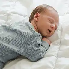 Neugeborenes Baby schläft friedlich auf weißer Bettwäsche und trägt ein hellblaues Langarm-Outfit.
