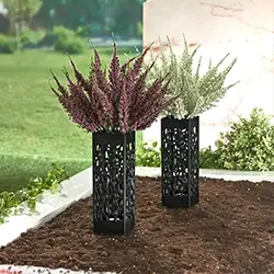 Zwei dekorative schwarze Vasen mit violetten und weißen Blumen in einer Gartenumgebung, auf Erde platziert, mit Grünpflanzen im Hintergrund.