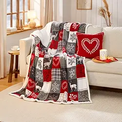 Gemusterte Wohndecke in Rot, Grau und Weiß mit Herz- und Hirschmotiven, dekorativ über Sofa und Sitzkissen in einem Wohnraum drapiert.