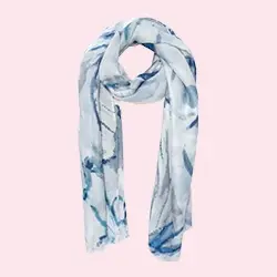 Une écharpe douce et blanche avec des motifs bleus de style aquarelle drapée en boucle sur un fond rose pâle.
