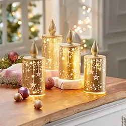 Vier goldfarbene Leuchtdekorationen mit ausgestanzten Sternmotiven auf einer Fensterbank, umgeben von Weihnachtskugeln und festlicher Dekoration.