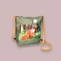 Grüne Tragetasche mit gelbem Trageriemen, auf der ein rotes Eichhörnchen abgebildet ist, das gerade frisst und eine Strickmütze mit Bommel trägt.